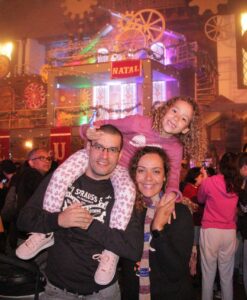 Pai com filha nos ombros e esposa ao lado, apreciando o Natal Luz em Gramado.