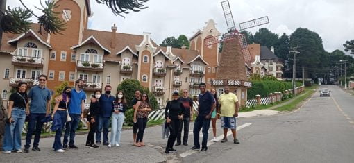 Grupo de turistas posando em frente a um edifício de estilo europeu com moinho de vento em Campos do Jordão