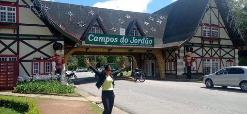 Turista sorridente posando em frente ao portal de entrada de Campos do Jordão, com decoração temática e bonecos de soldados.