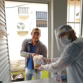 Cafeicultor da Chapada Diamantina entrega amostra de café para técnico de avaliação, com ambos sorrindo e o técnico usando equipamento de proteção.
