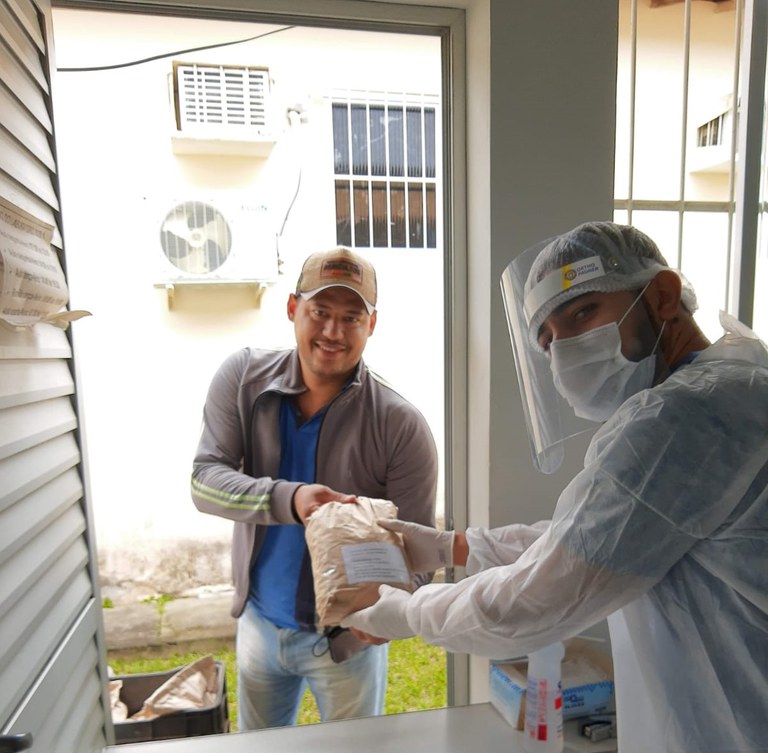 Cafeicultor da Chapada Diamantina entrega amostra de café para técnico de avaliação, com ambos sorrindo e o técnico usando equipamento de proteção.