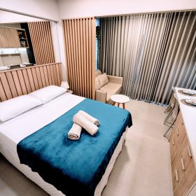 Interior do Studio 305 com cama de casal, sofá e cozinha americana no Barra Conceito